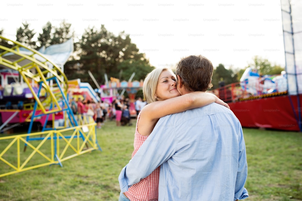 Casal de idosos se divertindo na feira de diversão, abraçando e beijando. Dia ensolarado de verão.