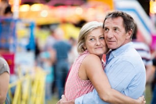 Casal de idosos se divertindo na feira de diversão, abraçando-se. Dia ensolarado de verão.