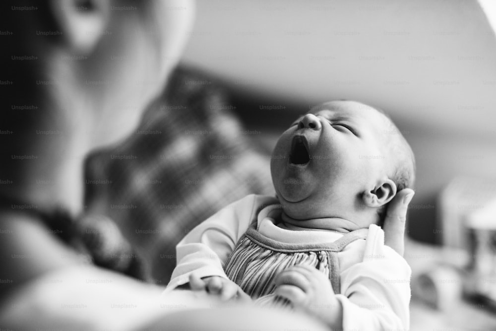 Jeune mère méconnaissable à la maison tenant sa fille nouveau-née en pleurs.