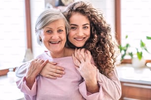 A teenage girl with mother or grandmother at home, hugging. Family and generations concept.