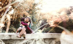 A portrait of young mother with a toddler daughter hugging and kissing in forest in autumn nature. Copy space.