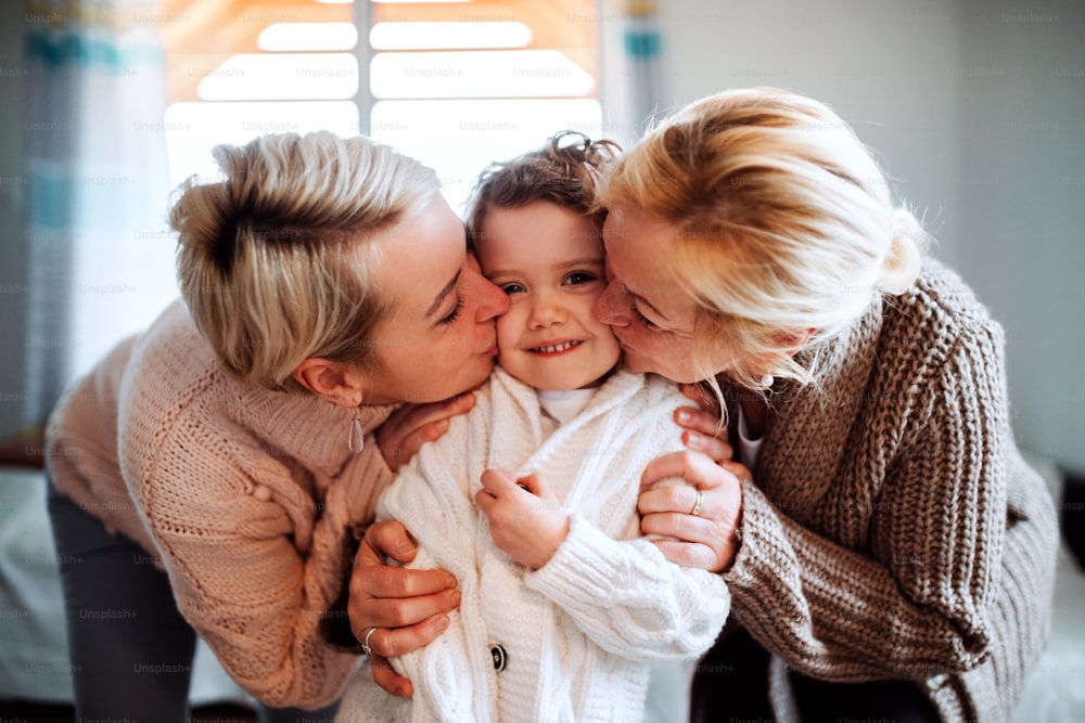 A portrait of happy small girl with mother and grandmother at home, kissing.