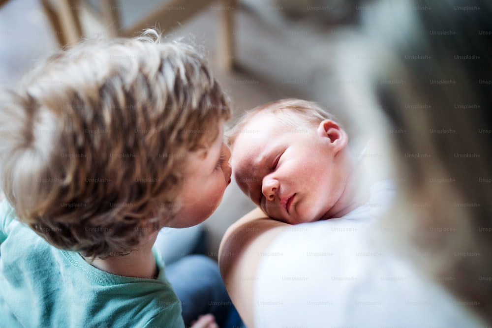 Un petit garçon embrassant un petit frère nouveau-né endormi à la maison, une mère le tenant.