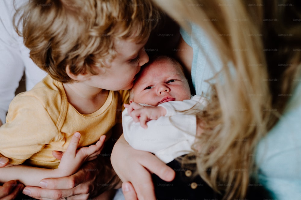 A small boy kissing a newborn baby brother at home, a mother holding him.