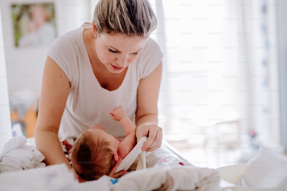 A front view of beautiful young mother looking after a newborn baby at home.