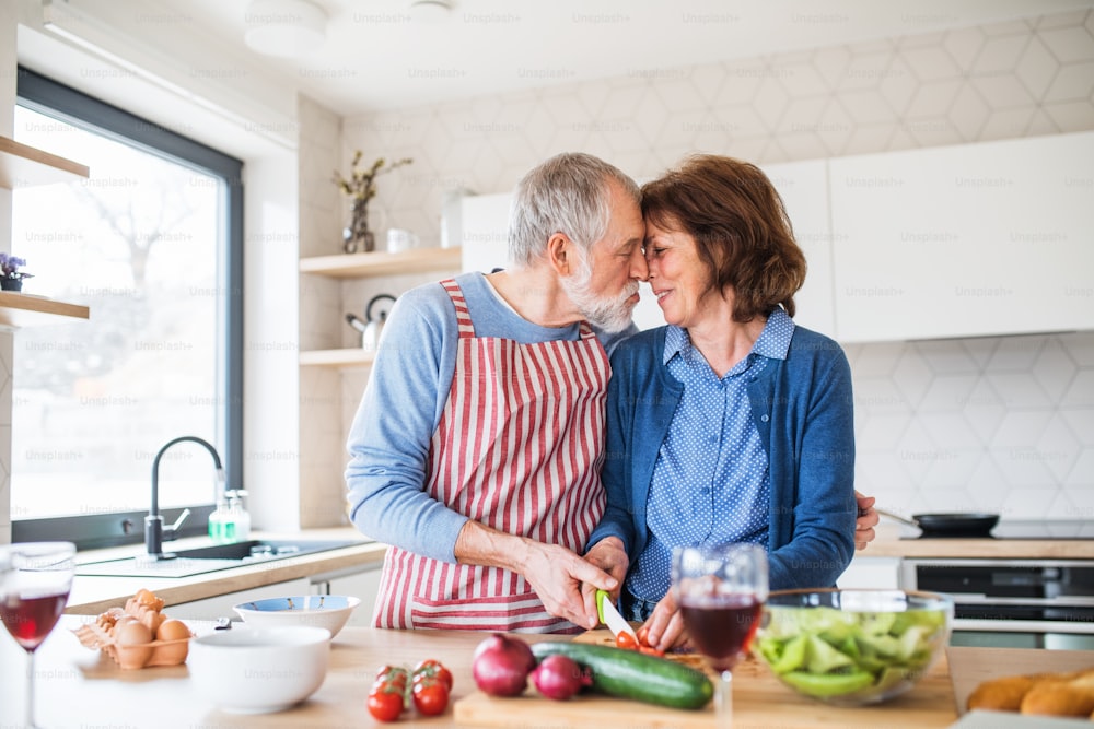 A portrait of happy senior couple in love indoors at home, cooking.