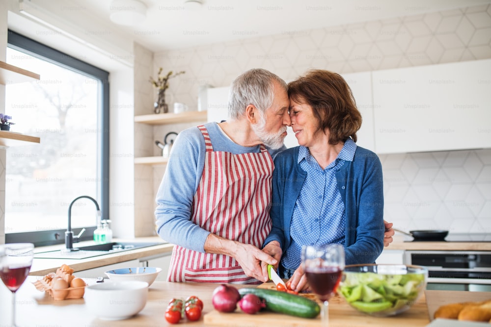 Ein Porträt eines glücklichen älteren Paares, das zu Hause verliebt ist und kocht.