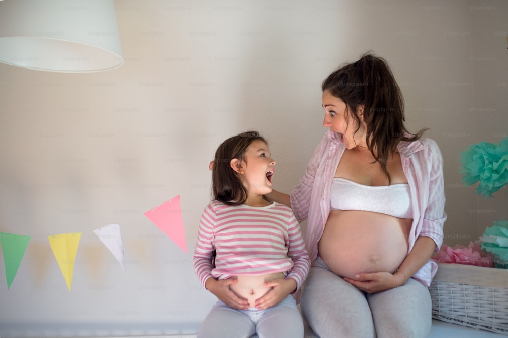 Retrato de mulher grávida com filha pequena dentro de casa em casa, se divertindo.