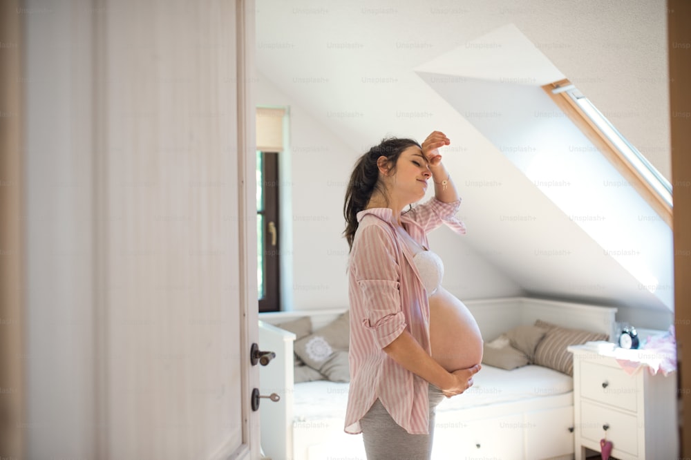 Retrato lateral de una mujer embarazada cansada en el interior de su casa, sosteniendo la cabeza.
