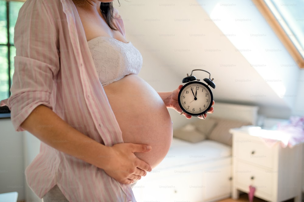 Donna incinta irriconoscibile con orologio impostato da cinque a dodici al chiuso a casa, concetto di data di scadenza.