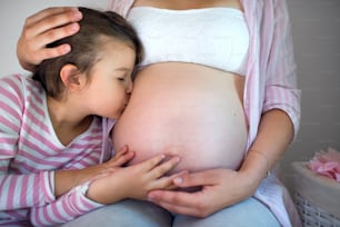 自宅の屋内で認識できない妊婦の腹にキスをする小さな女の子の側面図。