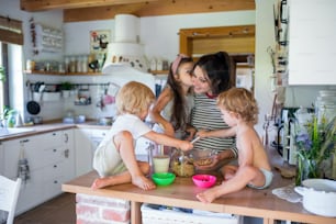 Happy pregnant woman with three small children indoors at home, preparing breakfast.