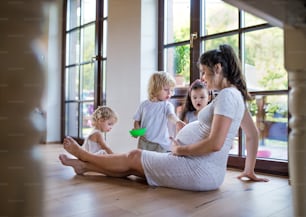 Happy pregnant woman with small children indoors at home, playing.