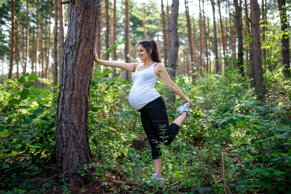 Side view portrait of happy pregnant woman outdoors in nature, doing exercise.