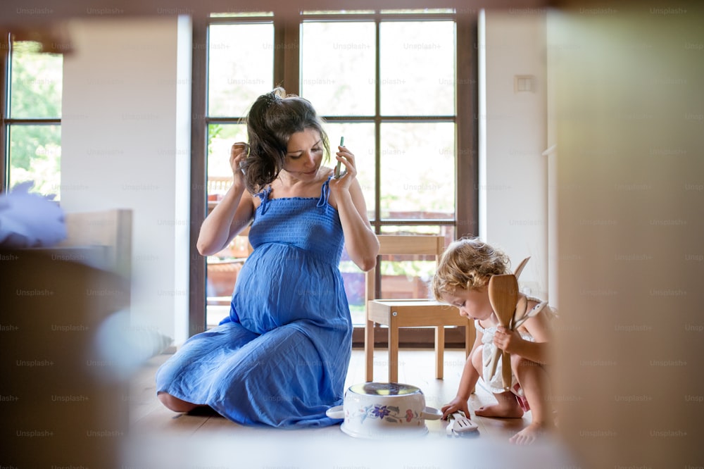 Happy pregnant woman with small child indoors at home, using smartphone.