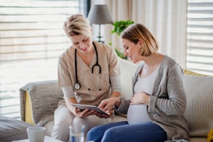 Un trabajador de la salud con una tableta hablando con una mujer embarazada en el interior de su casa.