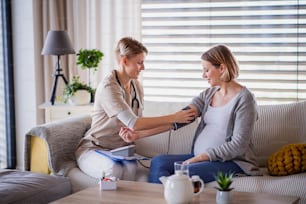 A healthcare worker examining pregnant woman indoors at home, checking blood pressure.