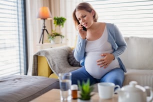Un retrato de una mujer embarazada con dolor en el interior de su casa, haciendo una llamada de emergencia.