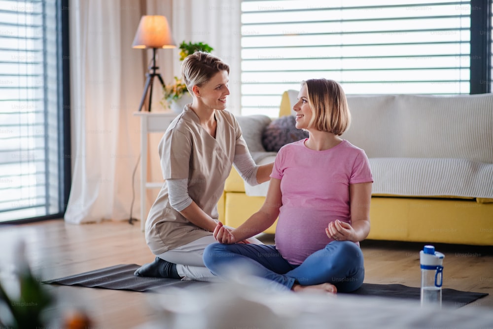 Trabajadora sanitaria y mujer embarazada activa en casa, haciendo ejercicio de yoga.