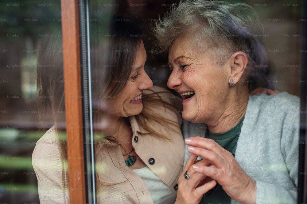 A close-up portrait of happy senior mother with adult daughter indoors at home, hugging and laughing.