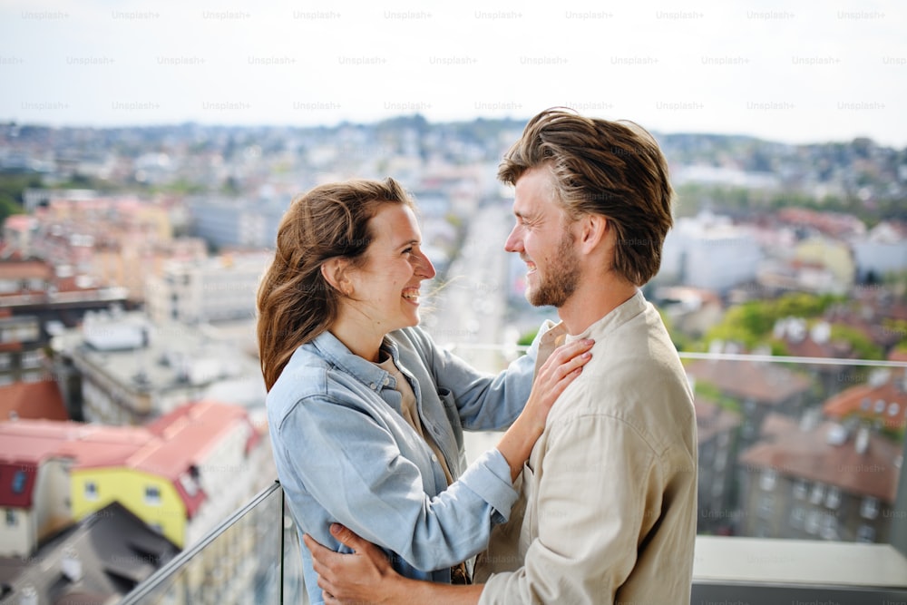 Una joven pareja feliz enamorada de pie al aire libre en el balcón de casa, mirándose el uno al otro.