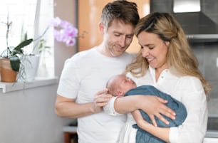 A smiling mother and father holding their newborn baby daughter at home