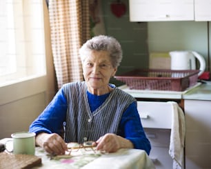 A mulher velha está sentada em sua cozinha estilo do país