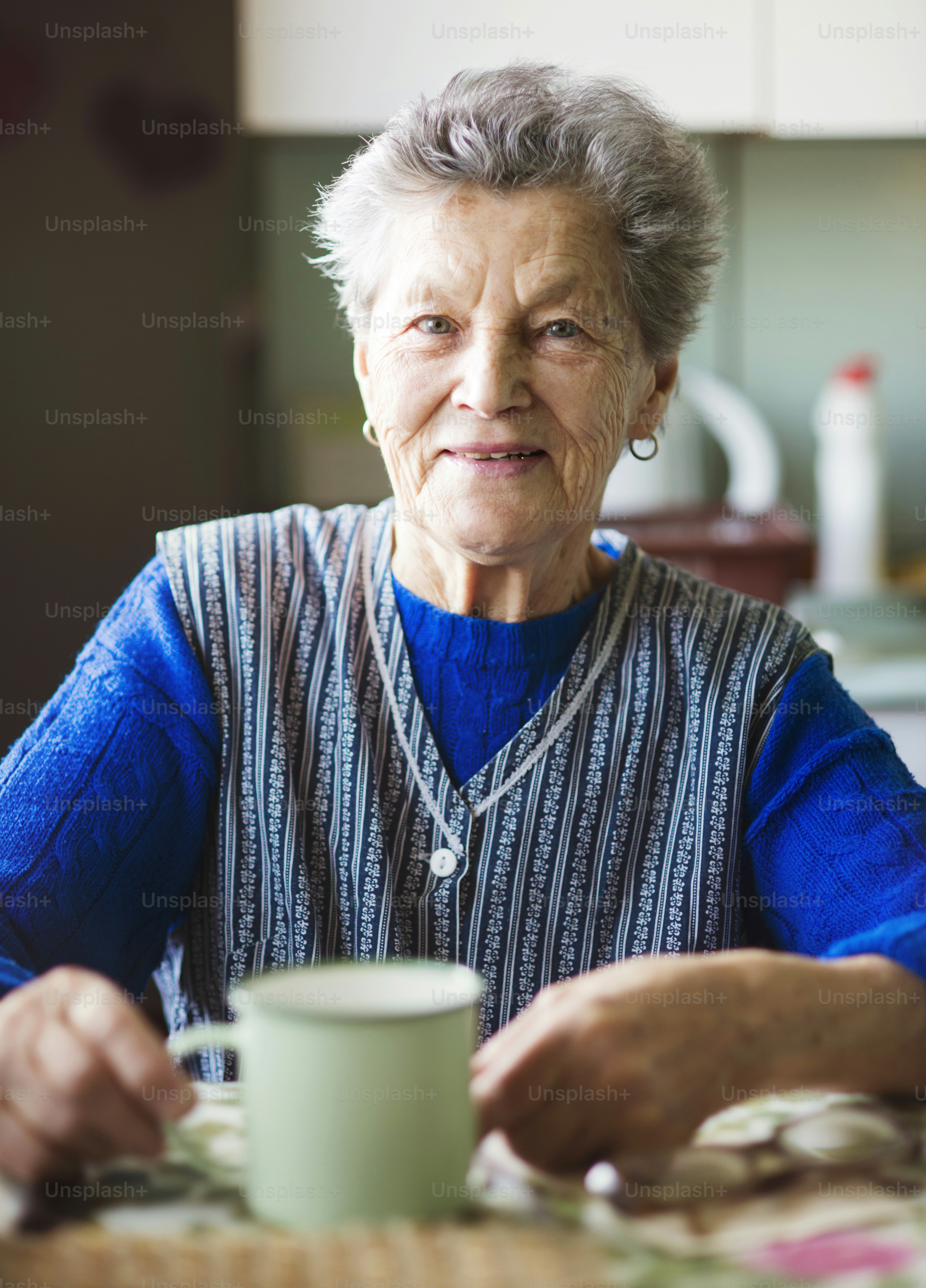 A mulher velha está bebendo chá em sua cozinha estilo do país