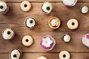 Table with various cupcakes, tarts and cookies. Studio shot on brown wooden background. Flat lay.