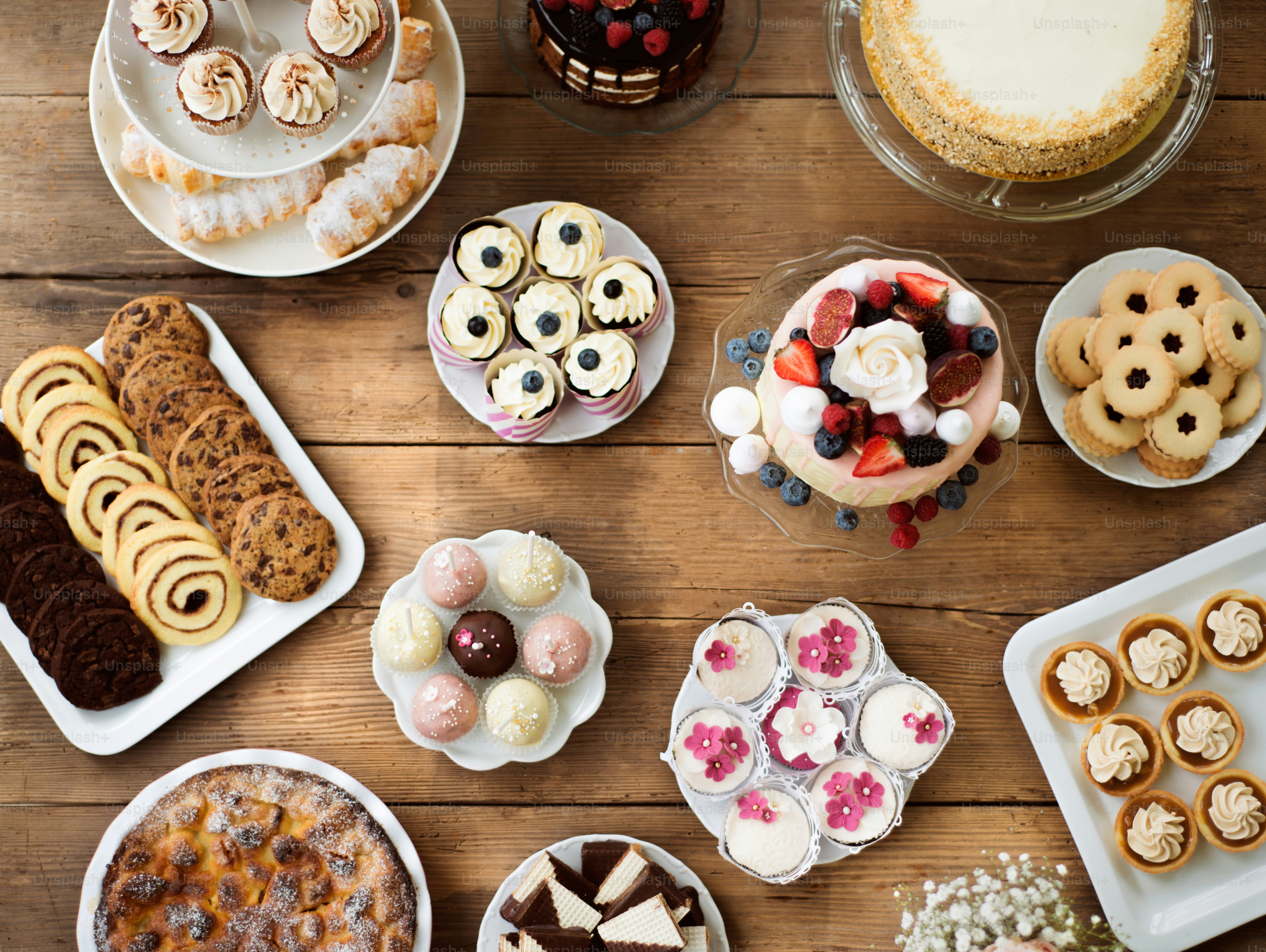 Meja dengan kue, pai, kue mangkuk, kue tart, dan cakepop. Bidikan studio dengan latar belakang kayu coklat. Rata berbaring.