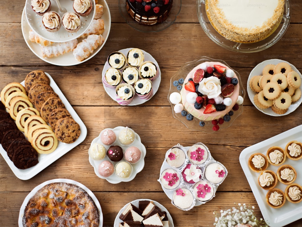 Tisch mit Kuchen, Torten, Cupcakes, Torten und Cakepops. Studioaufnahme auf braunem Holzhintergrund. Flache Verlegung.