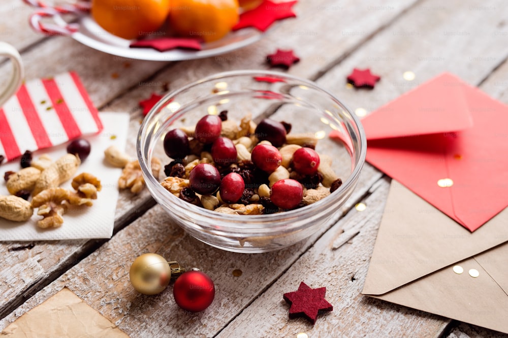 Christmas composition. Bowl with dried fruit, cranberries and nuts. Christmas cards and decorations. Various objects laid on table. Studio shot, wooden background.