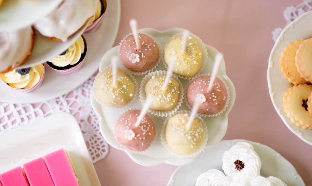 Table with white and pink cake pops on cakestand and various cakes. Candy bar.