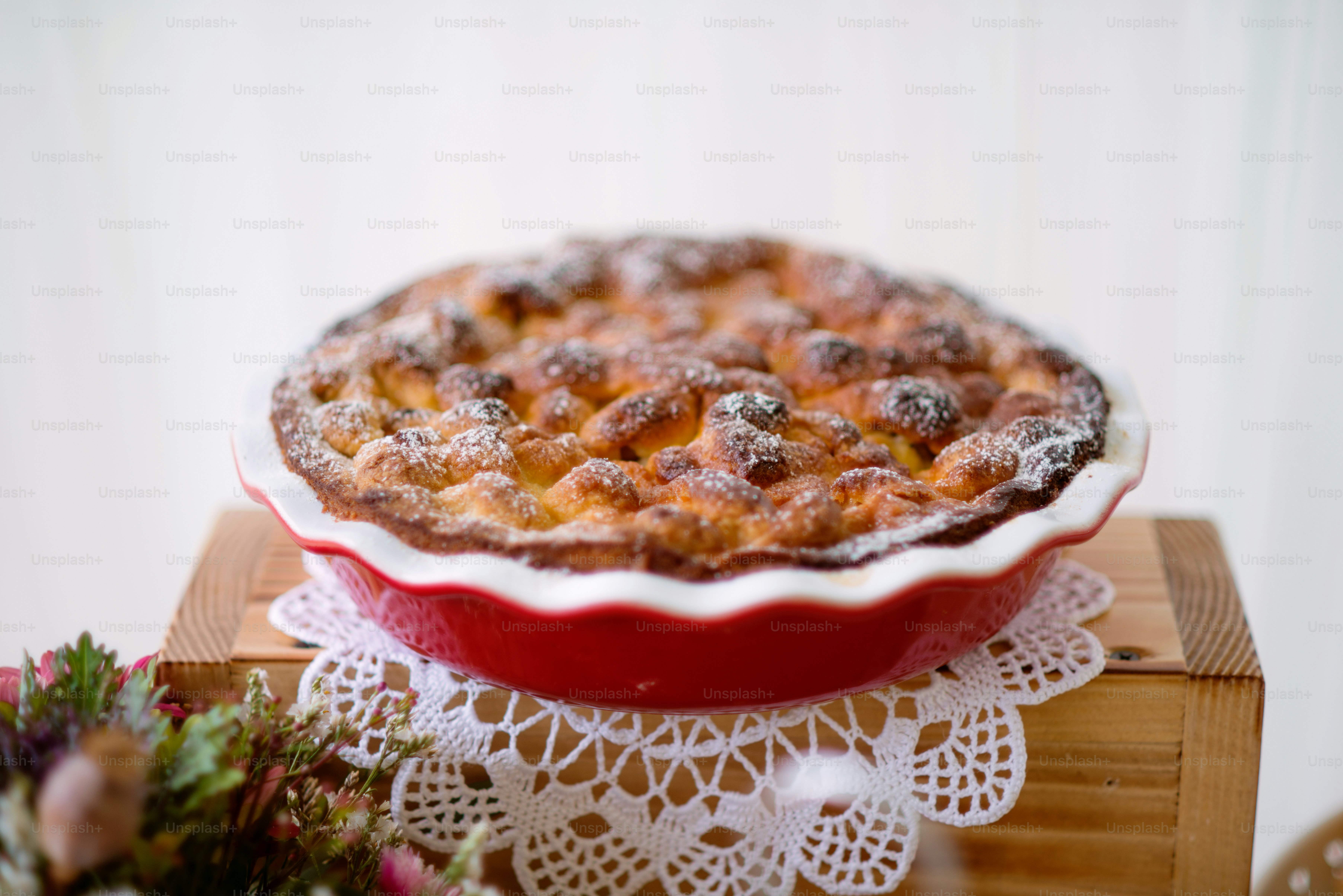 Tisch mit süßem Kuchen in rotem Porzellantablett auf Holzkiste und handgefertigter Spitze.