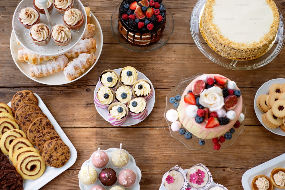 Table with cake, pies, cupcakes, tarts and cakepops. Studio shot on brown wooden background. Flat lay.