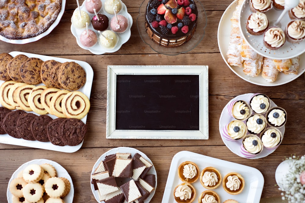 Table avec cadre, gâteau, cupcakes, tartes, biscuits et cakepops. Photo studio sur fond en bois brun. Espace de copie. Pose plate.