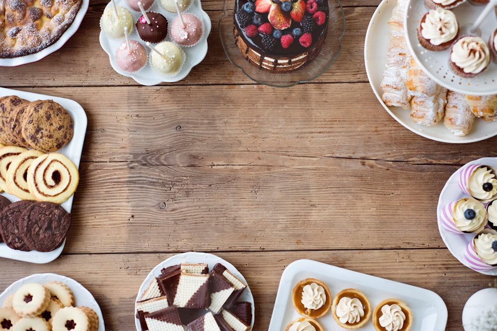 Table with cake, pie, cupcakes, tarts and cakepops. Frame composition. Studio shot on brown wooden background. Copy space. Flat lay.