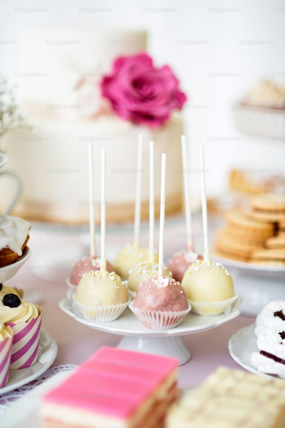 Table avec gâteaux blancs et roses pops sur le porte-gâteau et divers gâteaux. Barre chocolatée.