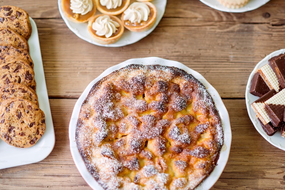 Table with sweet pie, tarts, wafers and chocolate chip cookies. Close up. Studio shot on brown wooden background. Flat lay.