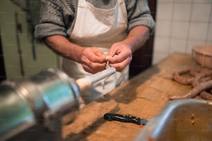 Homem irreconhecível fazendo salsichas da maneira tradicional usando enchimento de salsicha. Linguiça caseira.