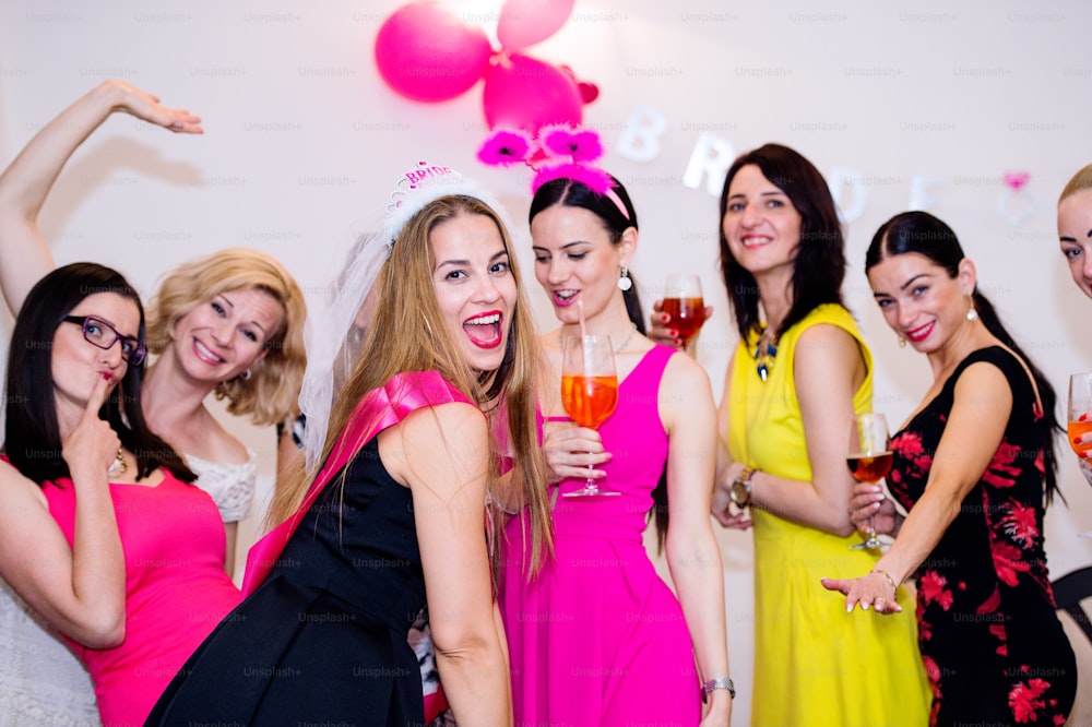 Novia alegre y damas de honor felices celebrando despedida de soltera con bebidas. Mujeres disfrutando de una despedida de soltera bailando.