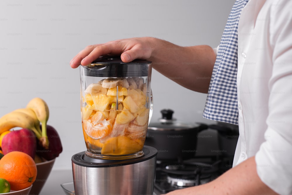 Un gros plan cadré d’un homme préparant un smoothie à partir de fruits frais dans un mélangeur ou un robot culinaire professionnel.