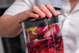 A close up cropped shot of man making smoothie from fresh fruits in professional blender or food processor.