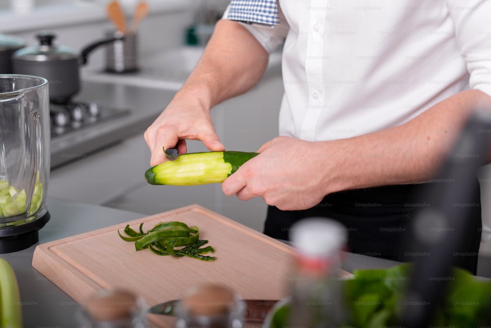 Un homme préparant un repas végétarien épluchant du concombre sur une planche à découper. Repas maison