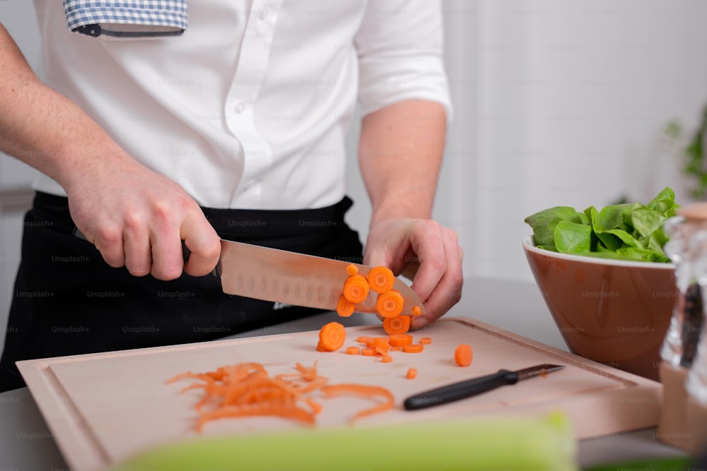 Um homem preparando refeição vegetariana cortando cenoura em tábua de corte. Refeição caseira