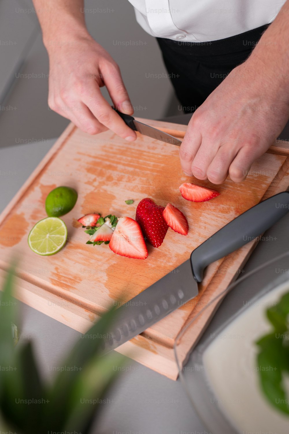 A man cutting strawberries and limes on chopping board.