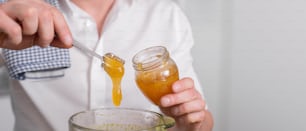 A close up cropped shot of man making smoothie and adding organic honey to blender or food processor.