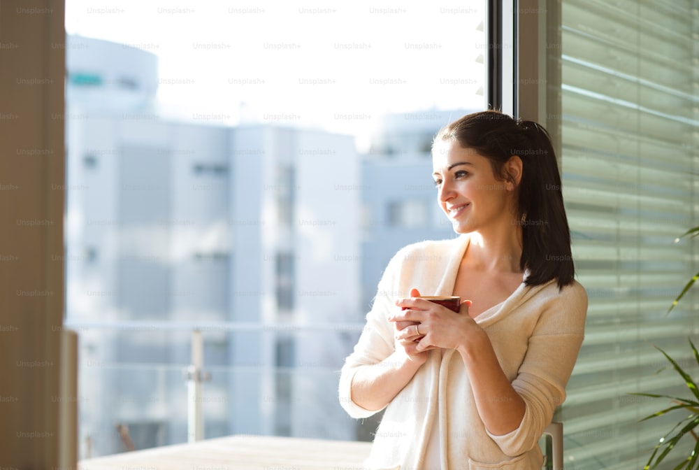 Beautiful young woman relaxing on balcony with city view holding cup of coffee or tea