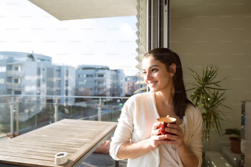 Hermosa joven relajándose en el balcón con vista a la ciudad sosteniendo una taza de café o té