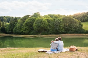Hermosa pareja de ancianos en el lago haciendo un picnic. Verde naturaleza soleada de verano.